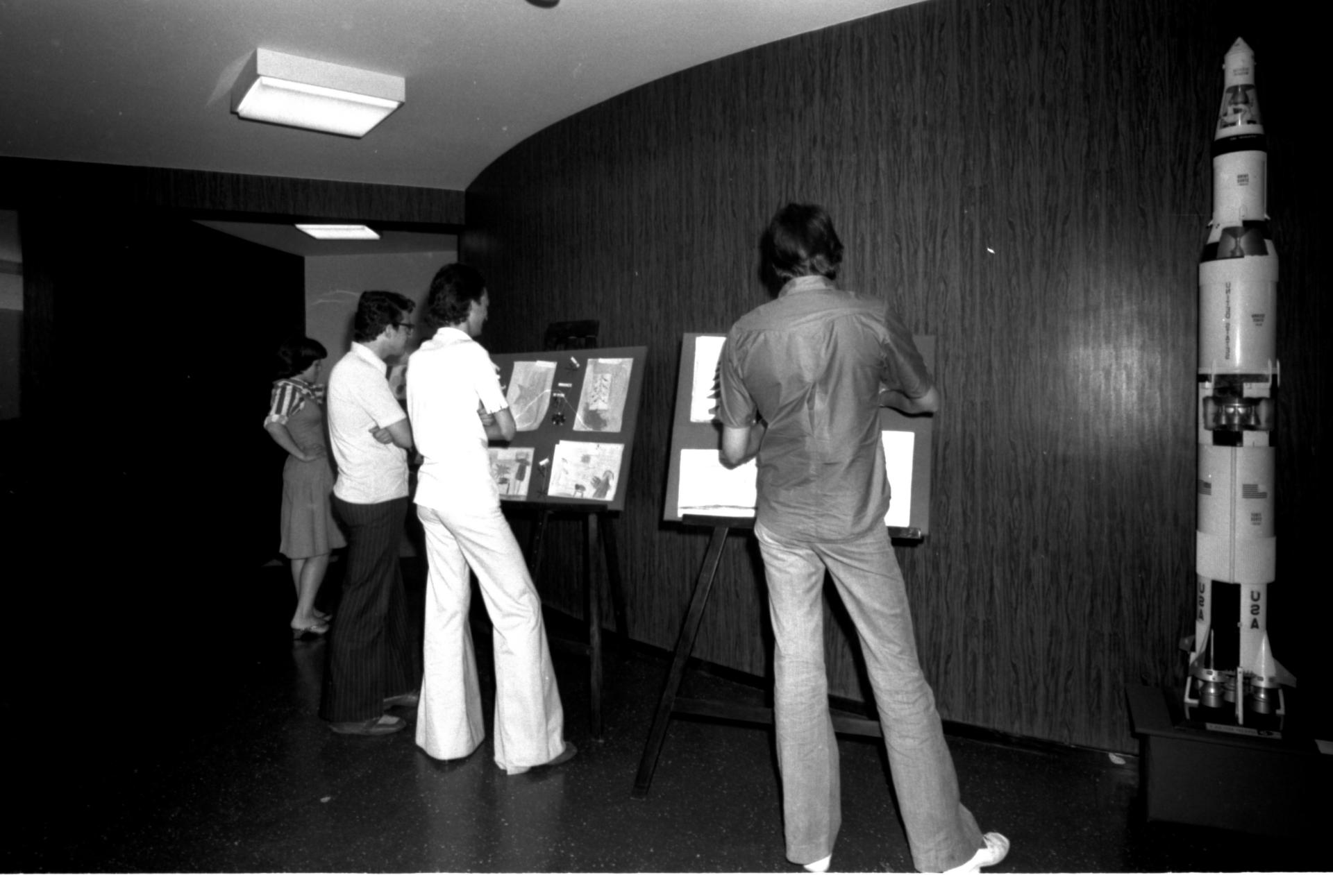 Foto preto e branca de pessoas olhando uma exposição no hall do Planetário