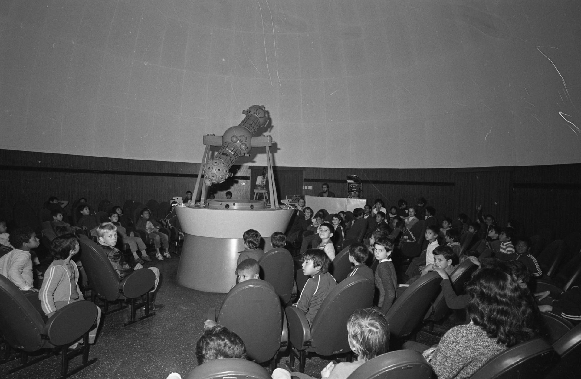 Foto preto e branca de diversas crianças sentadas na Sala de Projeção do Planetário