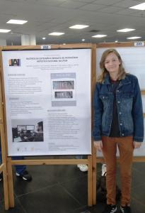 Fotografia vertical colorida de uma moça ao lado de um banner