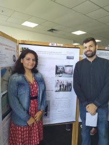 Fotografia vertical colorida de uma mulher e um homem em frente a um banner