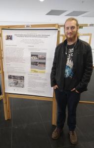 Fotografia vertical colorida de um jovem ao lado de um banner