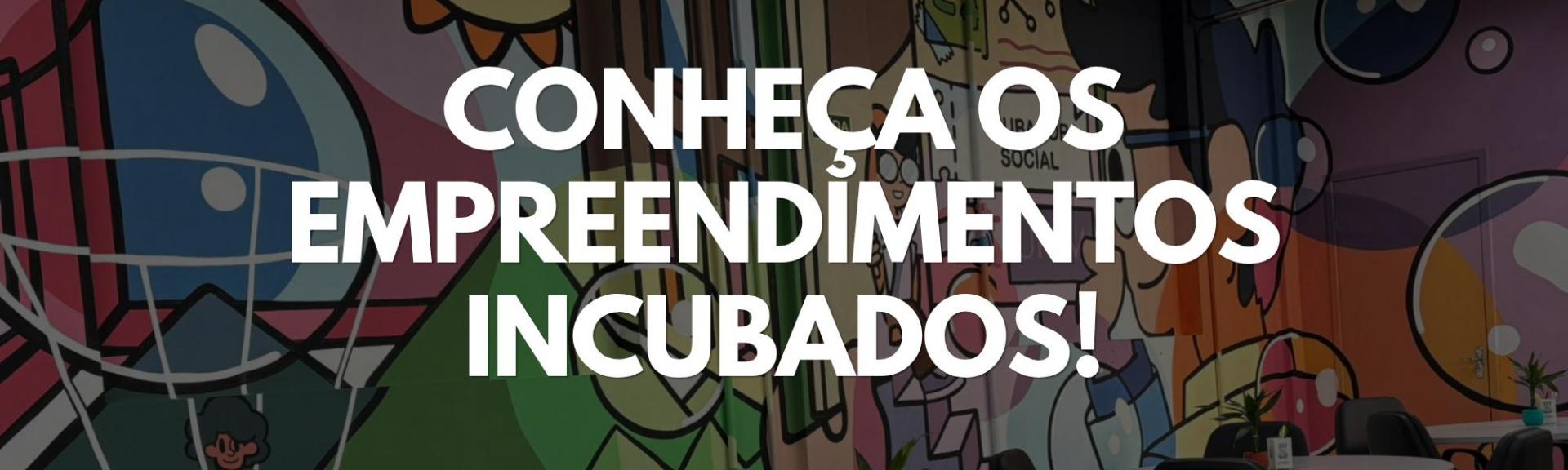 Imagem retangular. O fundo é composto por uma fotografia escurecida de uma parede interna do Hub IS, decorada com um grande mural colorido em estilo grafite, com ilustrações de rostos e formas geométricas. Centralizado na imagem, destaca-se o texto em letras grandes, brancas e em caixa alta: "CONHEÇA OS EMPREENDIMENTOS INCUBADOS!".