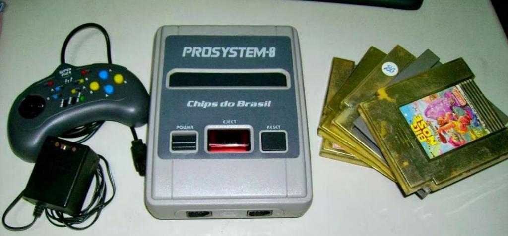 Imagem do Prosystem-8, clone do Nintendo 8-bits e fabricado pela Chips do Brasil em meados dos anos 90. Na foto há um controle em formato de meia lua, o videogame retangular com botões e espaço para alocar o cartucho e 4 cartuchos quadrados de jogos.