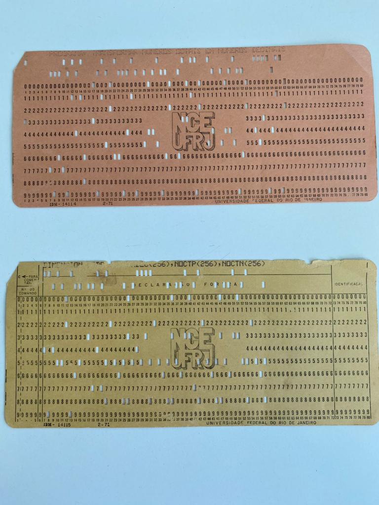 A imagem apresenta dois cartões perfurados da coleção pessoal da Professora e Tutora do PET S.I Patrícia Pitthan, que foram gentilmente concedidas por ela. Os cartões exibem, de forma centralizada, o logotipo do antigo Núcleo de Computação Eletrônica que agora é o Instituto Tércio Pacitti de Aplicações e Pesquisas Computacionais da Universidade Federal do Rio de Janeiro.