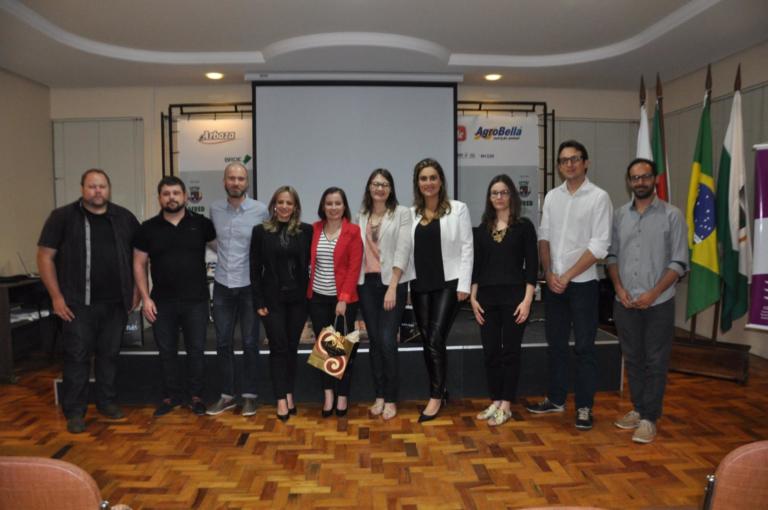 Diversas pessoas em pé em frente a um palco e tela de projeção