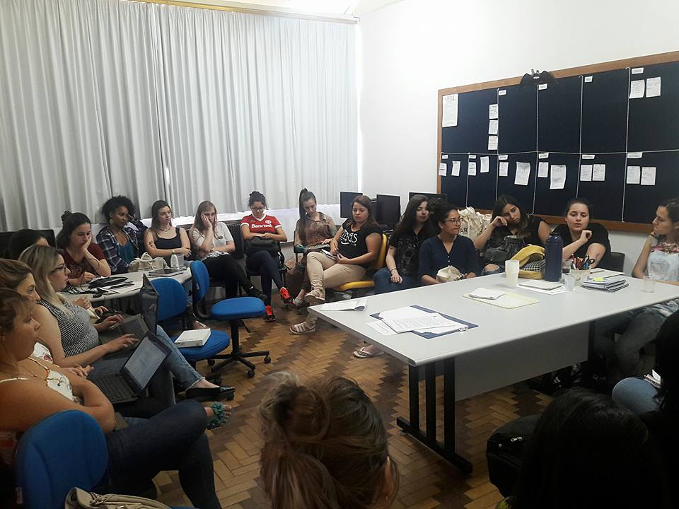 Sala com diversos estudantes sentados em formato circular