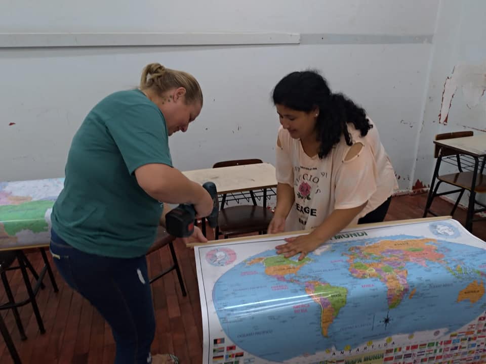 Duas acadêmicas do curso de Geografia - UFSM do Polo UAB Tapejara grampeando um mapa Mundo a uma mesa