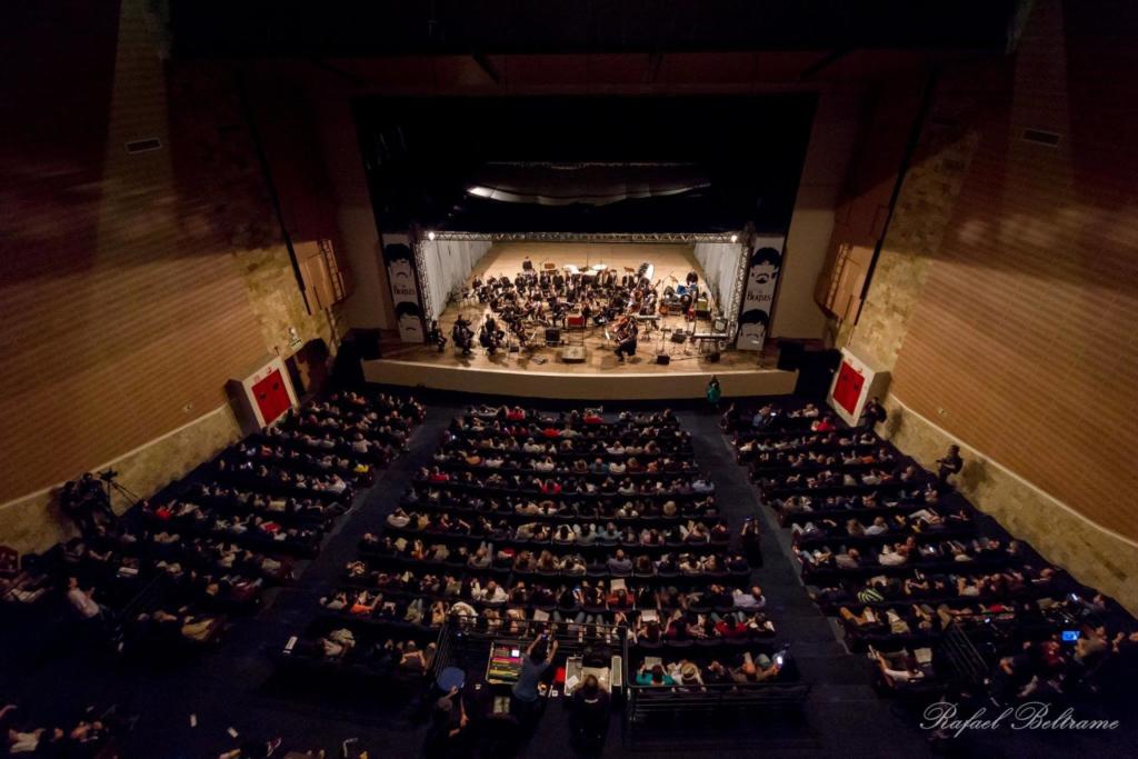 Fotografia tirada de cima da plateia cheia do Centro de Convenções. O palco está repleto de músicos.