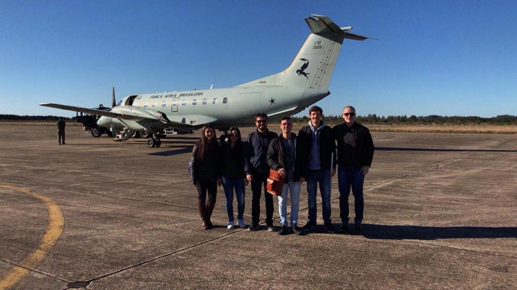Foto de seis alunos posicionados lado a lado, atrás deles há um avião.