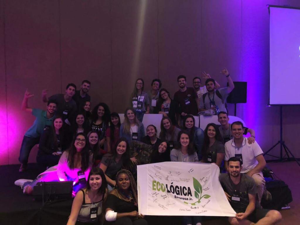 Alunos do projeto de extensão e empresa júnior ecologica seguram bandeira da empresa em um palco