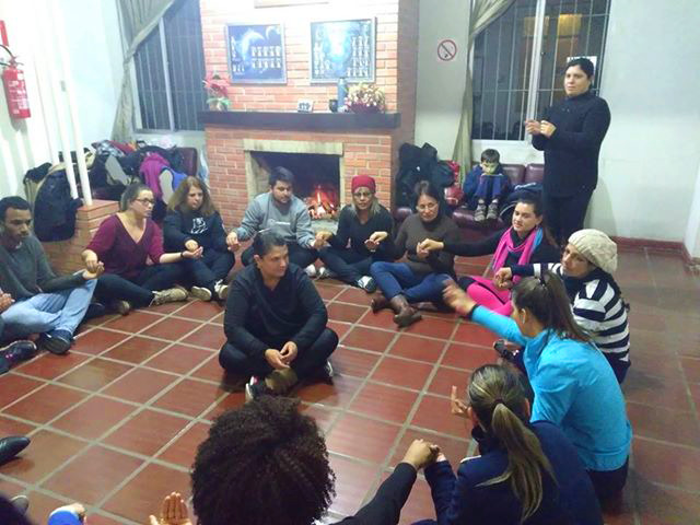 pessoas sentadas no chão em forma de circulo e outra pessoa sentada no meio