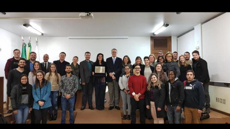 Foto de várias pessoas em pé sobre um palco, entre elas está o reitor ao centro da foto