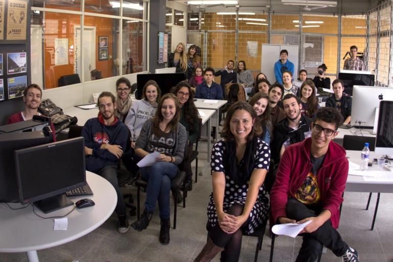 Grupo de pessoas sentada em uma sala com mesas e computadores.