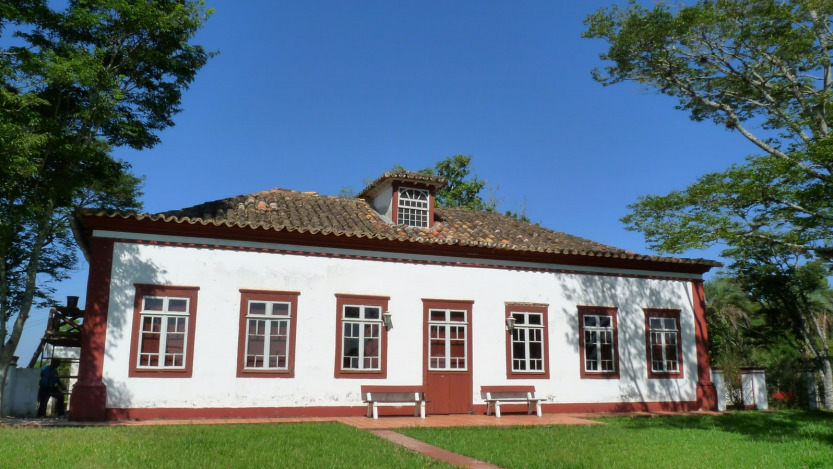 Casa colonial branca com porta e janelas vermelhas e árvores na volta