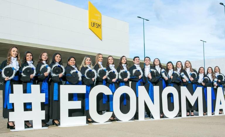 Formandos posicionados lado a lado atrás de um letreiro que diz "#Economia".