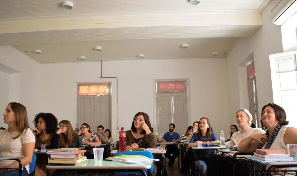 Foto de uma sala de aula, na sala tem vários alunos, maioritariamente mulheres, que estão sentados em suas classes.
