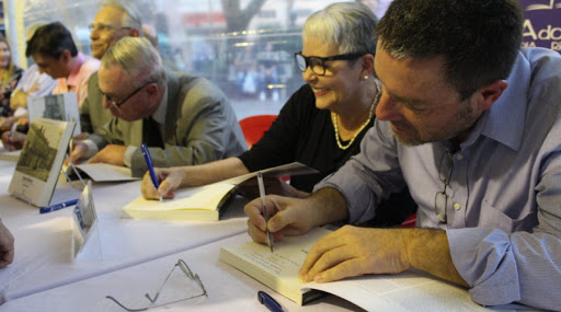 Foto de duas pessoas assinando em um livro.