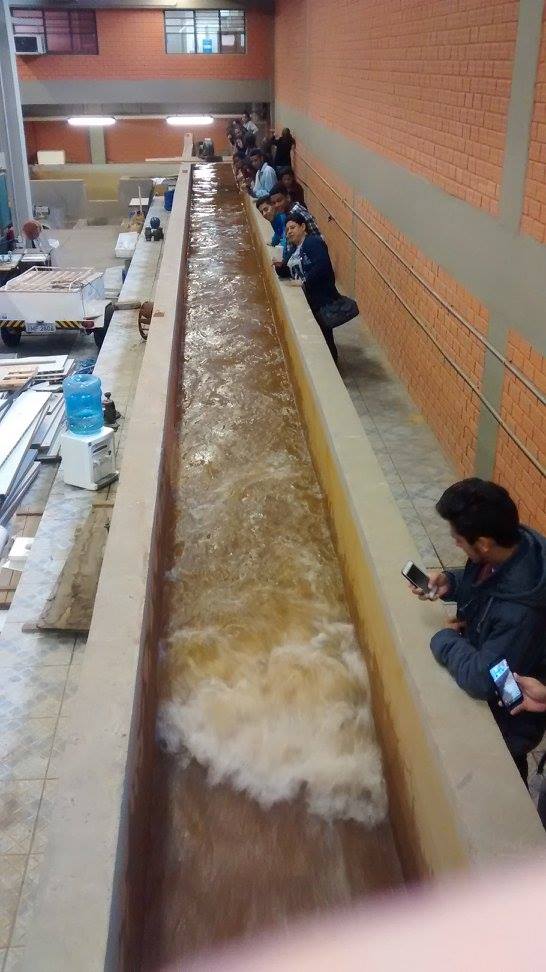 Foto de uma canaleta onde escorre água, alguns alunos estão ao redor dela observando.