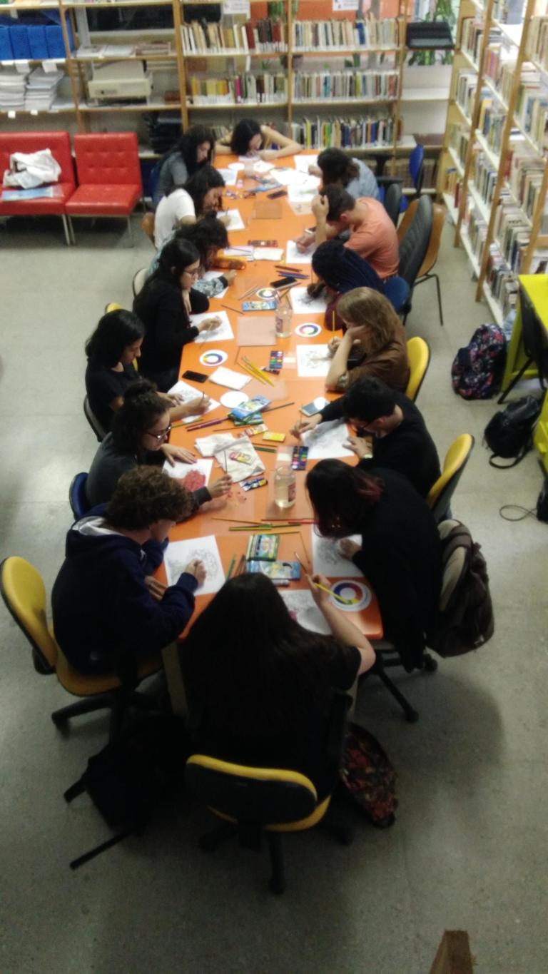Estudantes de Produção editorial sentadas em uma mesa retangular, realizando as ativides de uma das oficinas de criação