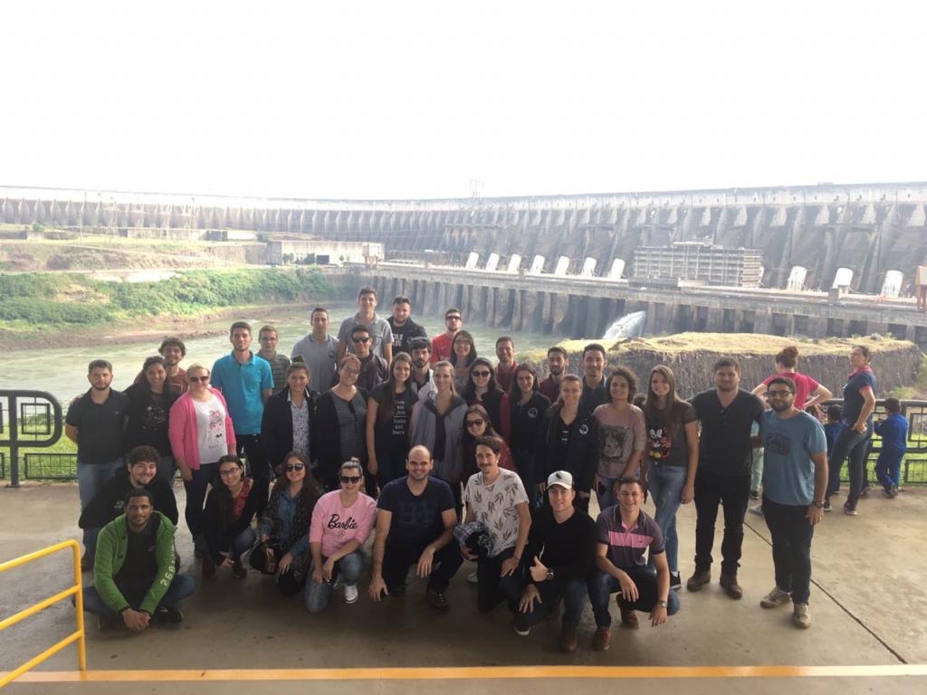 Alunos e professores em primeiro plano e atrás a usina hidrelétrica de Itaipu