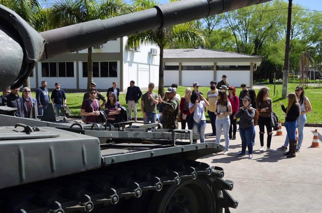 Foto de alguns alunos em um local aberto e militar, no lado esquerdo da foto tem um canhão.