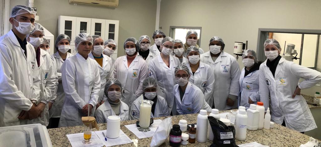 Várias pessoas vestindo jaleco, touca e máscara branca em frente a uma bancada de laboratório