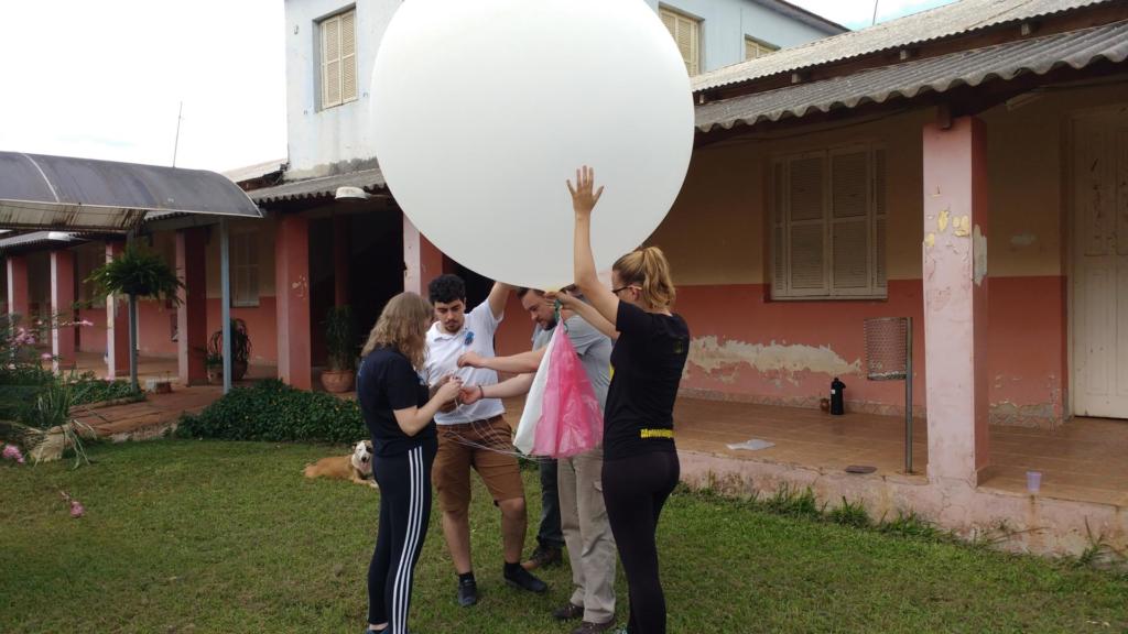 Foto de cinco pessoas que seguram um balão m.etereológico
