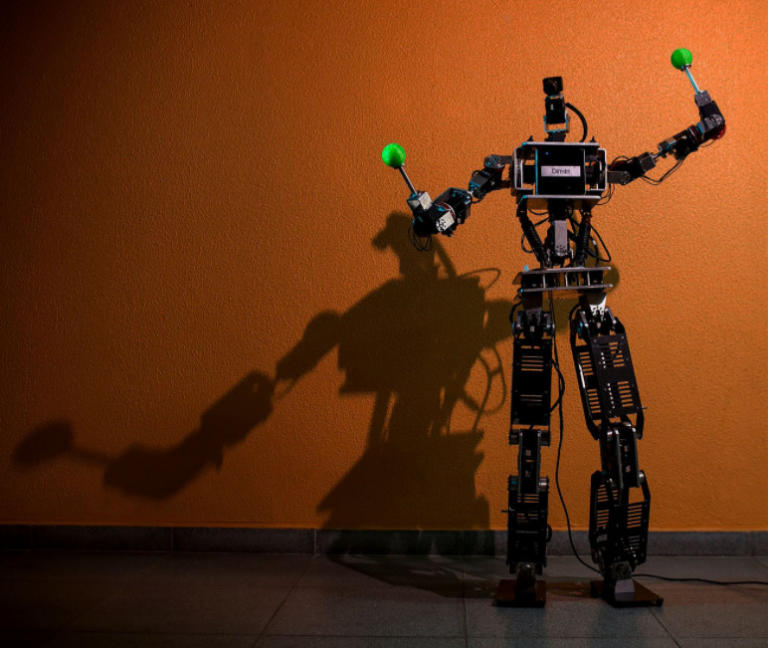 foto de um robô com os braços para cima em uma parede marrom