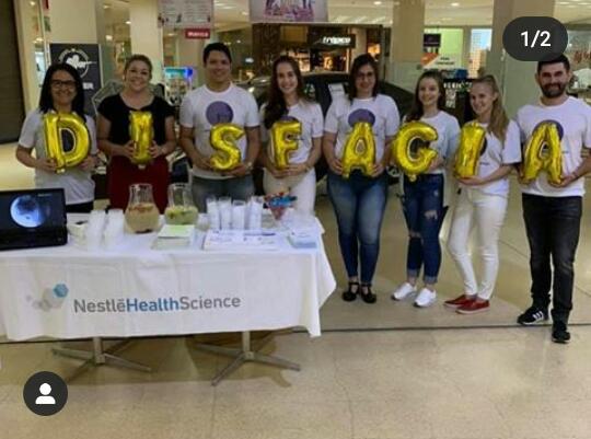 Foto de oito pessoas posicionadas lado a lado, cada uma delas segura um balão dourado em formato de letras que formam a palavra "Disfagia".