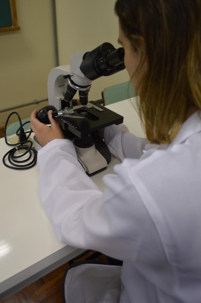 em um laboratório de microbiologia, uma mulher olha através de um microscópio