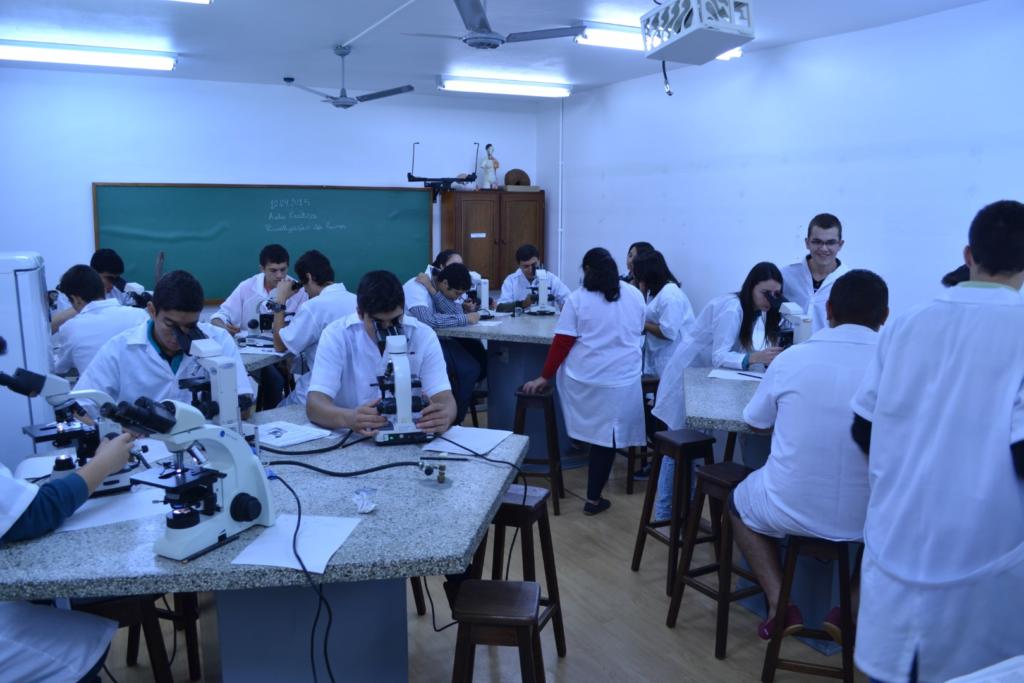 Laboratório com diversas pessoas usando jaleco branco e debruçadas sobre bancadas com equipamentos e estetoscópios