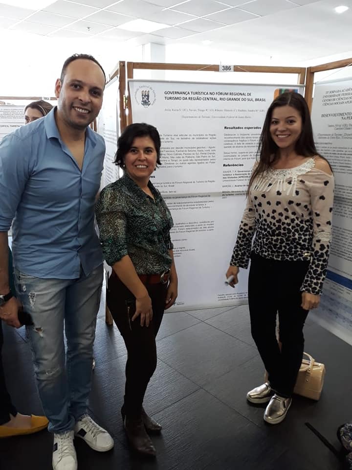 Três pessoas em pé em torno de banner da JAI