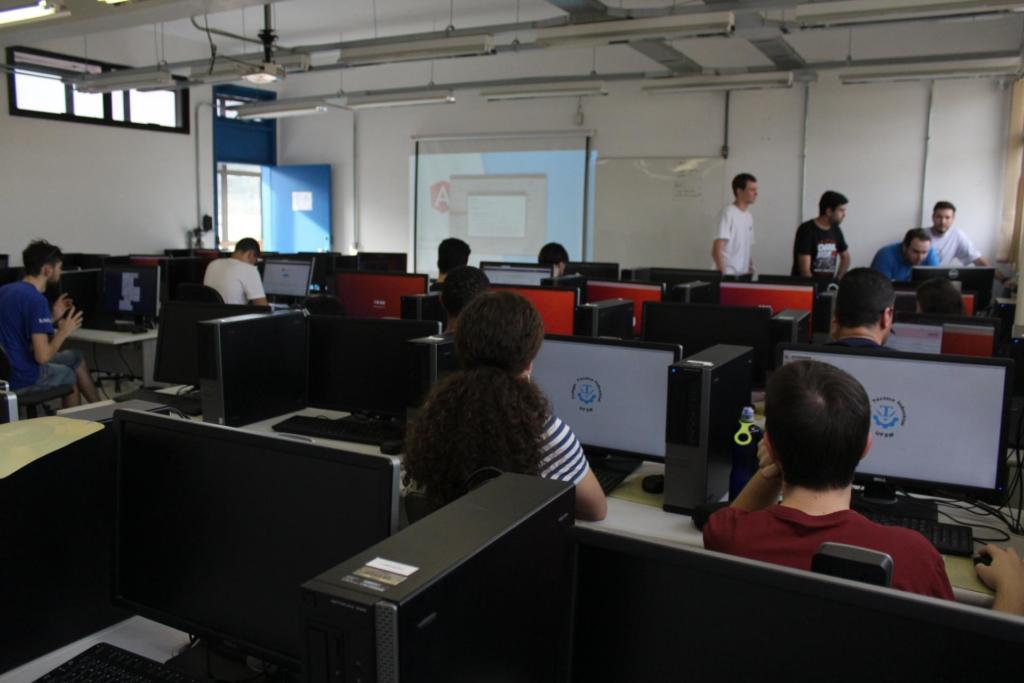 Foto de um sala com alguns computadores e alguns alunos.