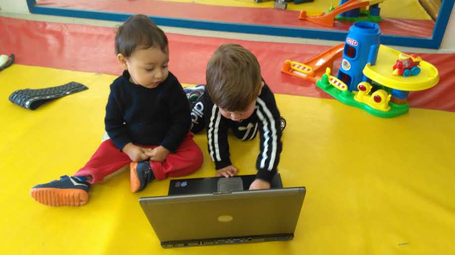 Duas crianças sentadas no chão mexendo em notebook