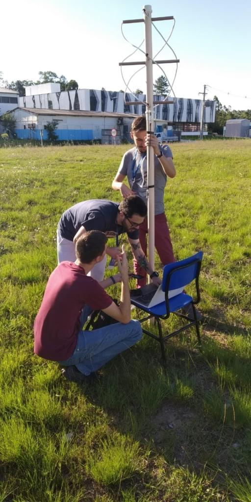 Três pesoas em torno de uma antena em gramado