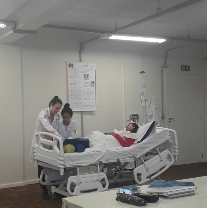 duas mulheres de pé mexendo em uma outra mulher deitada em uma cama hospitalar