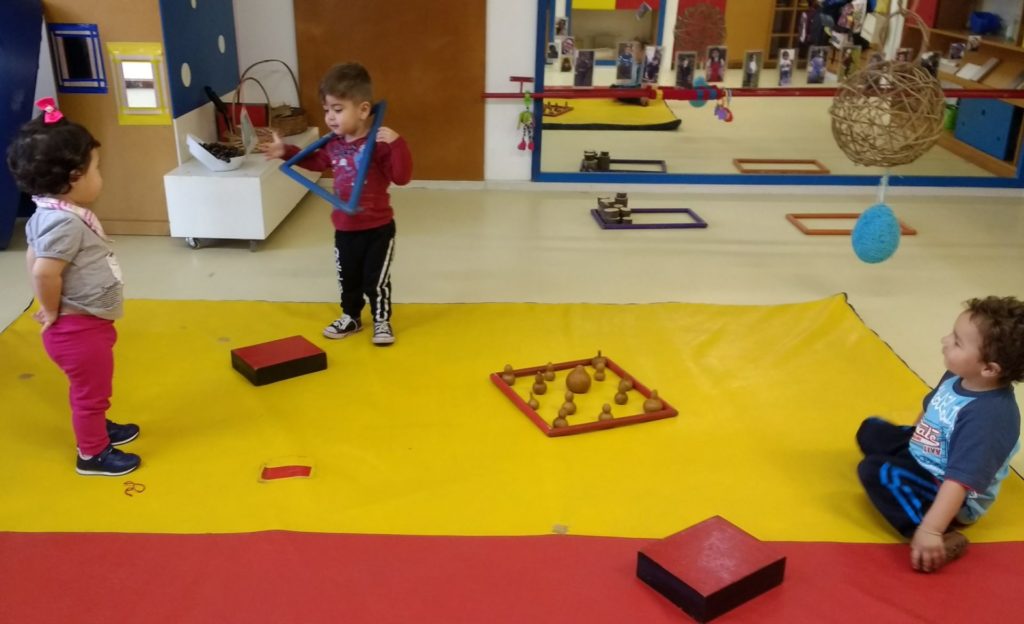 Crianças brincando em sala com brinquedos e tapete vermelho e amarelo