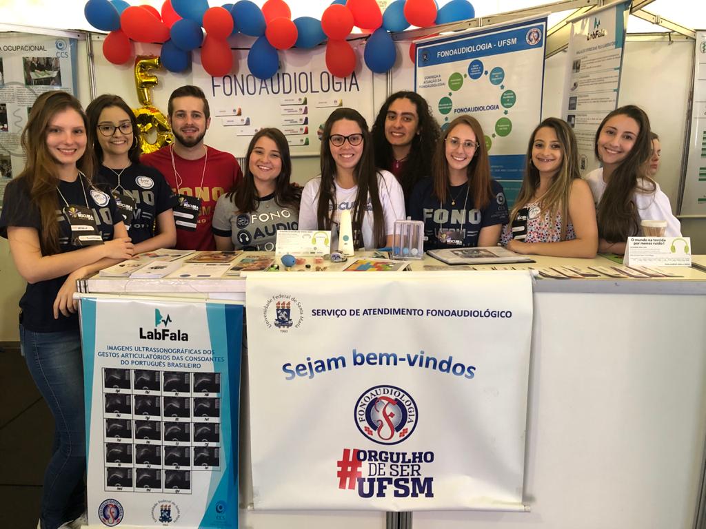 Diversos estudantes atrás de uma banca em stand do Descubra