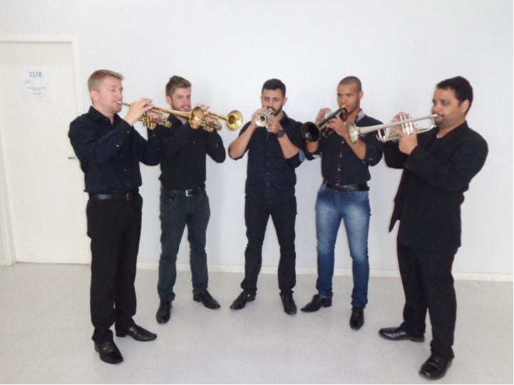 Cinco homens vestidos de preto tocando trompete
