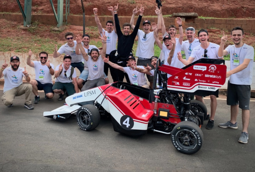 Carro de competição vermelho e branco com equipe celebrando ao fundo