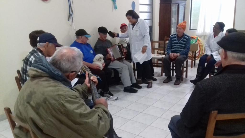 Foto de alguns idosos sentados em círculo, um deles segura uma gaita.
