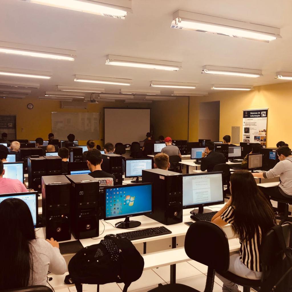 Foto de uma sala ampla com muitos computadores e alguns alunos.