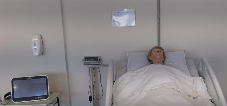 um quarto com uma cama hospitalar com um manequim deitado simulando uma pessoa