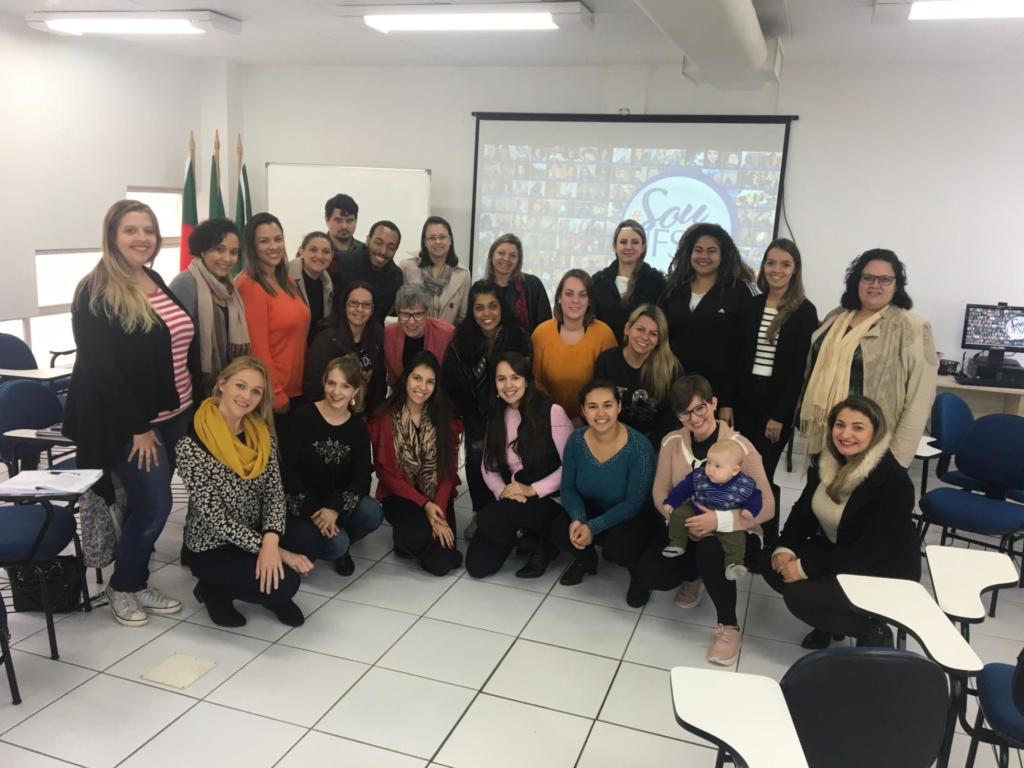Foto de várias pessoas reunidas, atrás delas um telão.