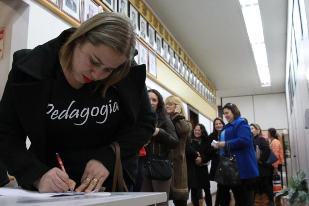 Foto de várias pessoas em uma fila, ao primeiro plano uma mulher que assina um papel.