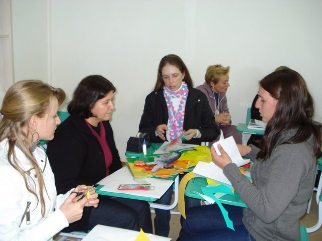 Foto de algumas mulheres sentadas ao redor de uma classe, fazendo trabalhos artesanais.