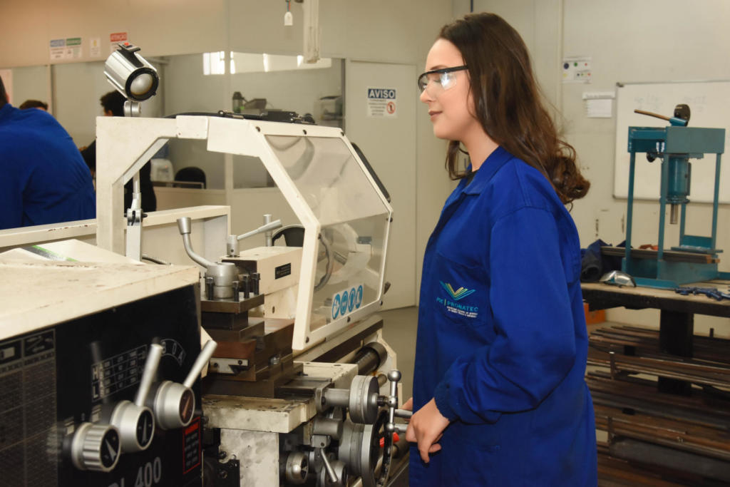 Mulher vestida de jaleco azul escuro trabalhando em torno mecânico