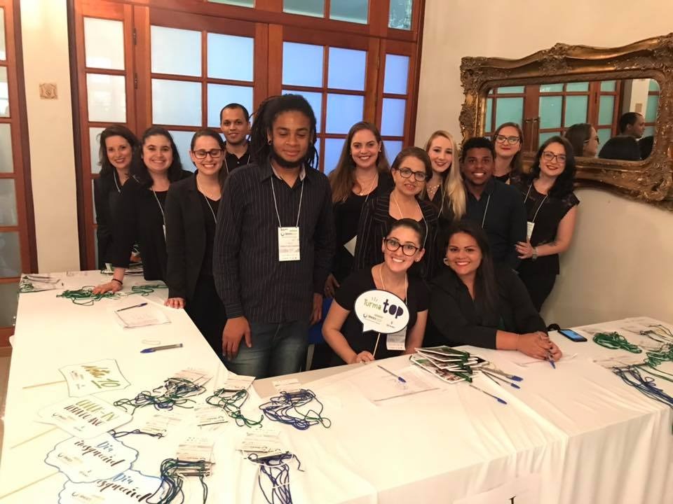 Foto de diversas pessoas uniformizadas atrás de uma mesa de recepção de evento