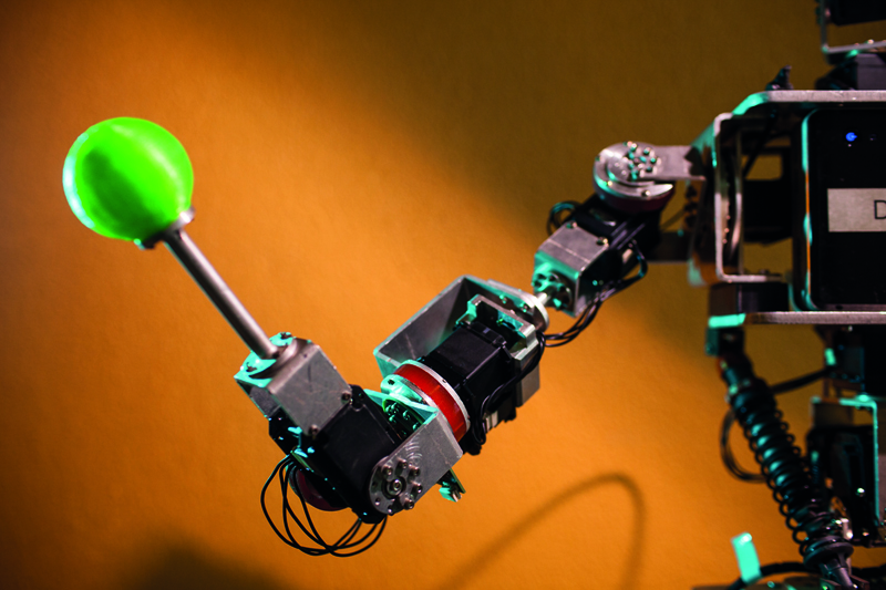 Detalhe do braço do robô Dimitri, que mostra a parte da série elástica em vermelho. Na mão do robô há um objeto verde de ponta arredondada.
