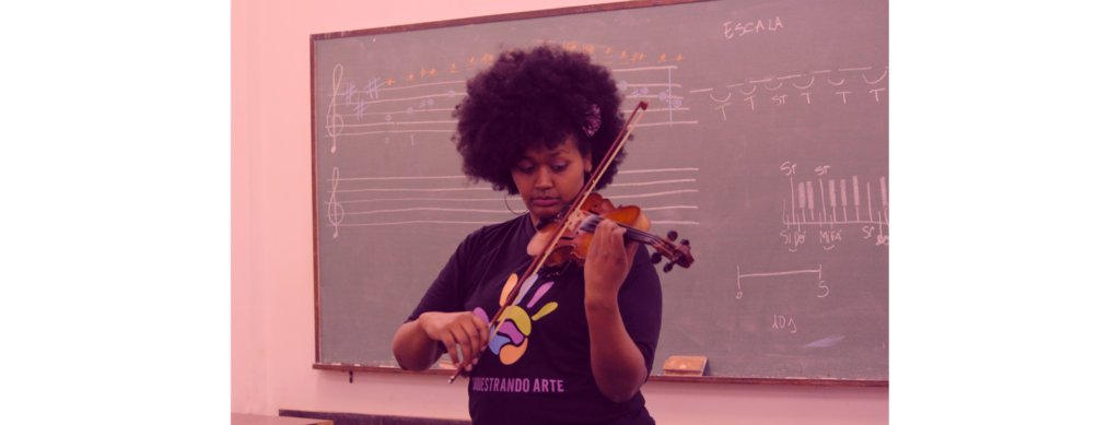 Em primeiro plano, moça toca violino. Ao fundo, quadro com partituras escritas com giz